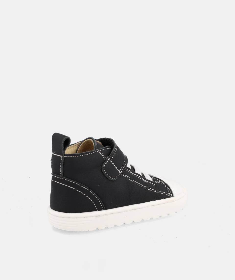 chaussure montante noire avec velcro, lacets élastiques blancs et semelle blanche