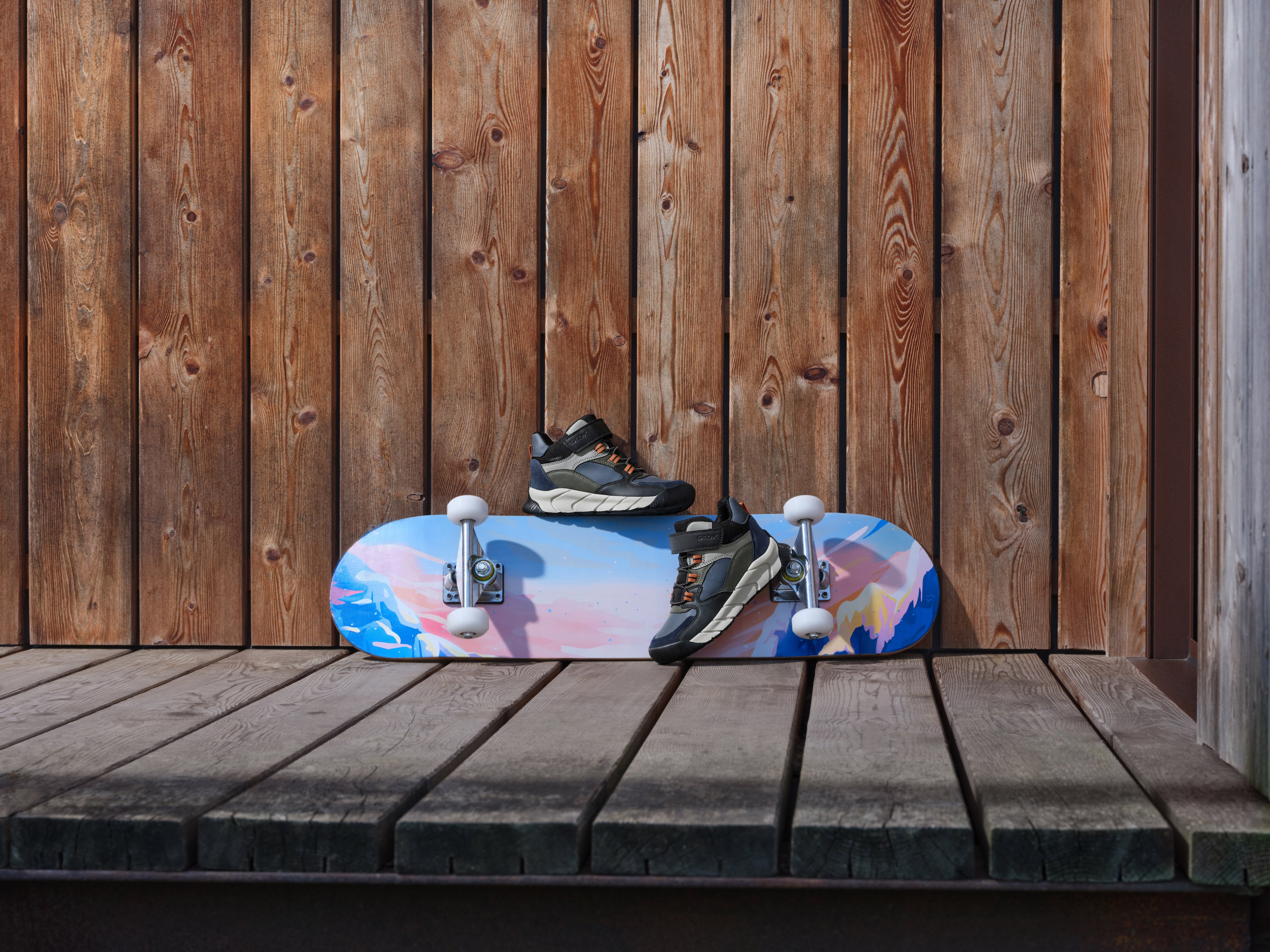 Bottines Geox mi-saison pour garçons, devant un mur en bois, sur un skateboard.