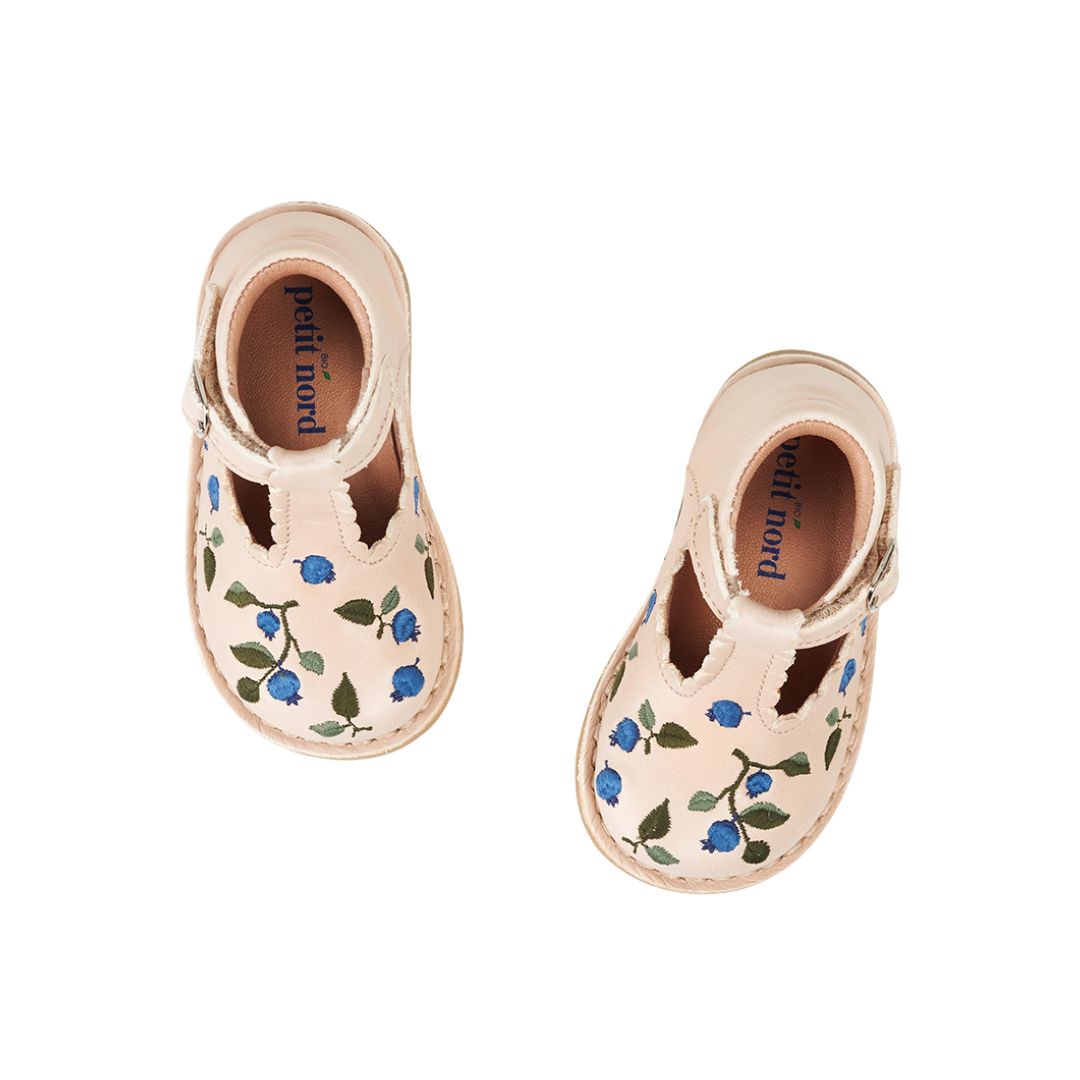 Chaussure semi-ouverte pour enfant, ton crème, avec détails de broderies de bleuets. Attache velcro, boucle décorative.