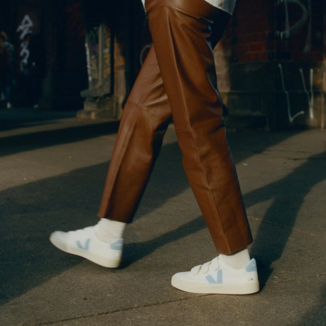 Une personne porte des VEJA blanche et bleu ciel avec trois velcros.