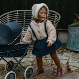 Une fillette debout jour avec une poussette et porte des chaussures Petit Nord couleur prune.