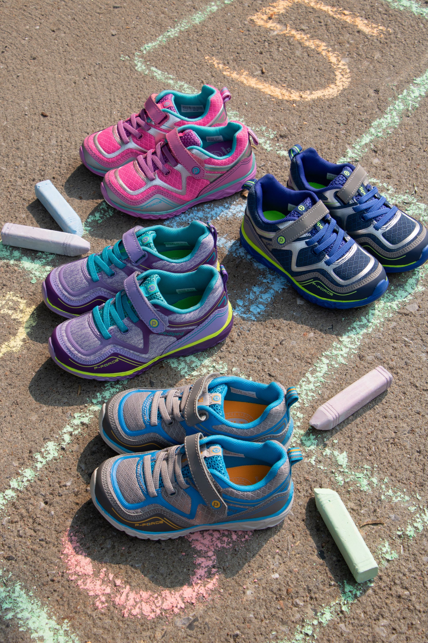 Des chaussures sport pour enfants de couleur rose, bleu, mauve, sur un sol avec dessin de marelle.