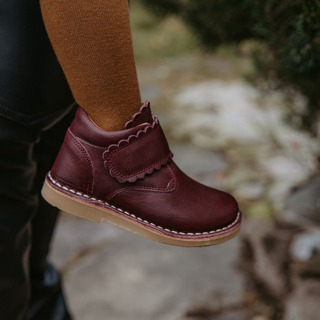 Une petite fille porte des collants jaune et des chaussures Petit Nord couleur prune à velcro