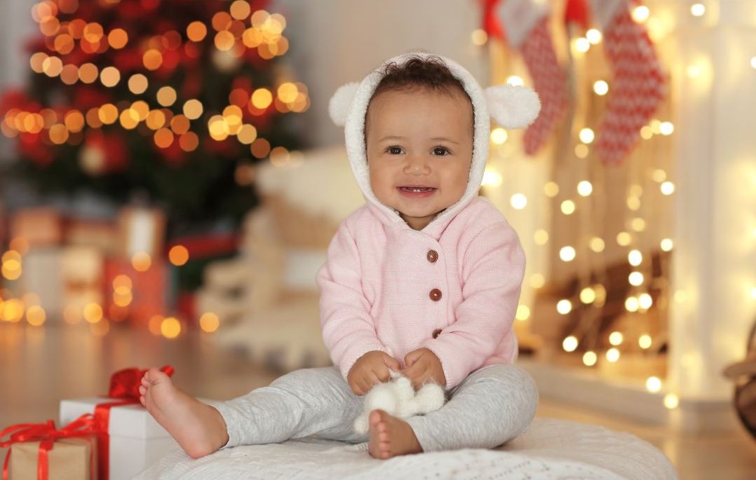Un bébé assis devant un sapin à côté de cadeaux de Noël