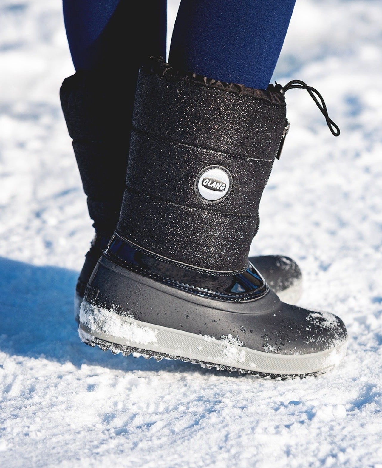 Un enfant porte une botte Olang noire dans la neige 