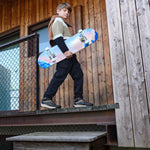 Un garçon tient un skateboard dans ces mains et porte aux pieds des belles bottines Geox mi-saison de couleur marine, noire et orange. 