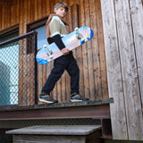 Un garçon tient un skateboard dans ces mains et porte aux pieds des belles bottines Geox mi-saison de couleur marine, noire et orange. 