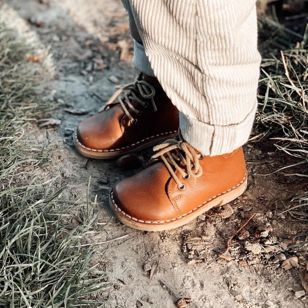Un garçon dehors porte des chaussures cognac Petit Nord avec lacets et pantalon beige