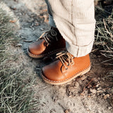 Un garçon dehors porte des chaussures cognac Petit Nord avec lacets et pantalon beige