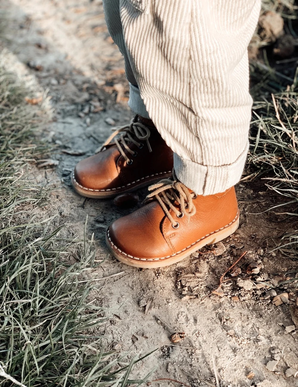 Un garçon dehors porte des chaussures cognac Petit Nord avec lacets et pantalon beige