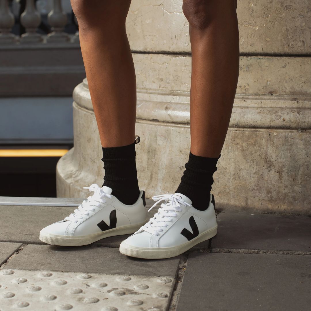 Une personne porte des Veja blanches et noires avec lacets. 