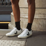 Une personne porte des Veja blanches et noires avec lacets. 