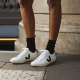 Une personne porte des Veja blanches et noires avec lacets. 