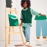 Un enfant debout devant un tableau, tient un pinceau et porte des chaussures Veja blanche et verte