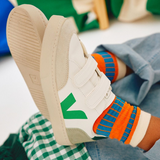 Un enfant porte des chaussures Veja blanche et verte avec velcro.